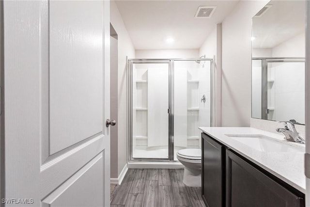 bathroom with hardwood / wood-style flooring, vanity, toilet, and walk in shower