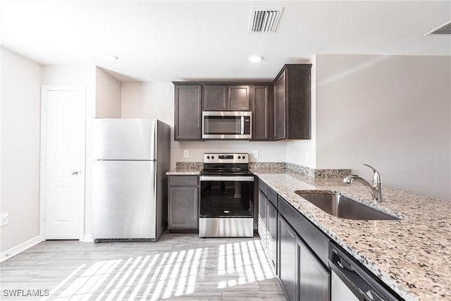 kitchen featuring dark brown cabinetry, stainless steel appliances, light stone countertops, and sink