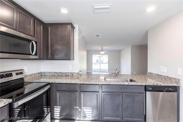 kitchen with light stone counters, stainless steel appliances, sink, and dark brown cabinets