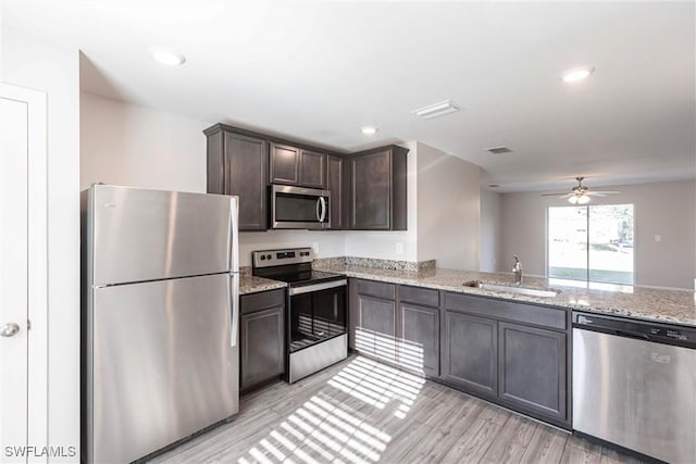 kitchen with sink, stainless steel appliances, light stone counters, dark brown cabinetry, and light wood-type flooring