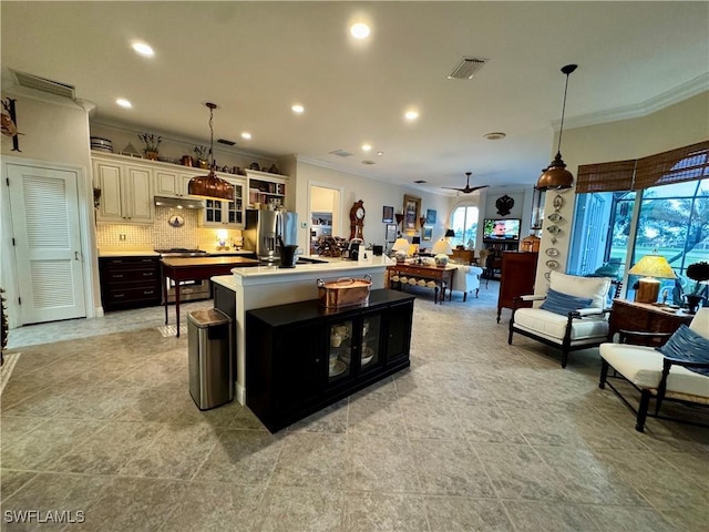 kitchen with tasteful backsplash, hanging light fixtures, stainless steel fridge with ice dispenser, ornamental molding, and a kitchen island with sink