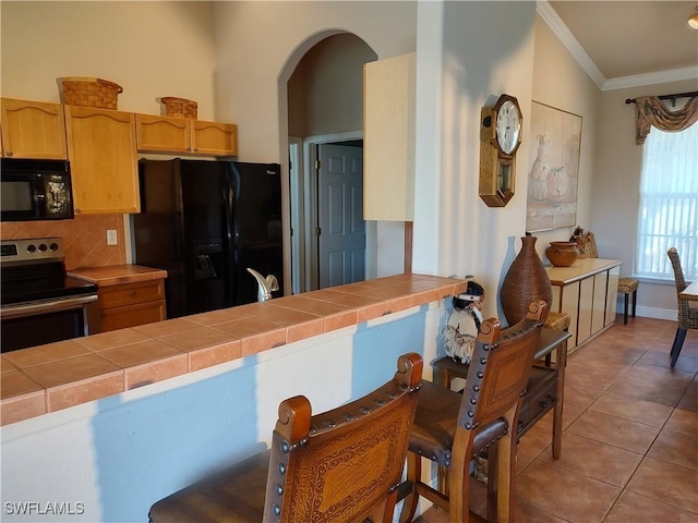 kitchen featuring ornamental molding, light tile patterned flooring, tile countertops, and black appliances