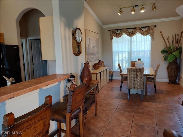 dining room featuring arched walkways, dark tile patterned flooring, ornamental molding, and baseboards