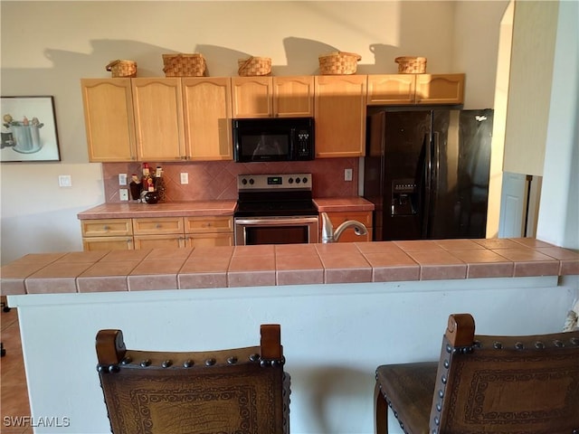 kitchen with tile counters, decorative backsplash, a peninsula, black appliances, and light brown cabinets