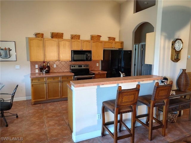 kitchen with arched walkways, tile patterned flooring, tile counters, black appliances, and tasteful backsplash