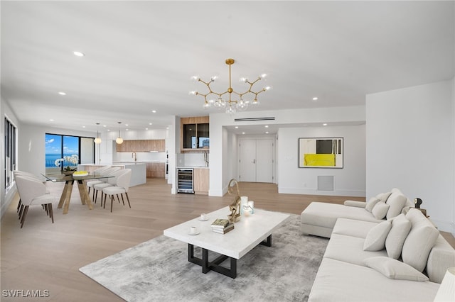 living room featuring an inviting chandelier, sink, beverage cooler, and light hardwood / wood-style flooring