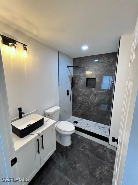 bathroom with tiled shower, vanity, and toilet