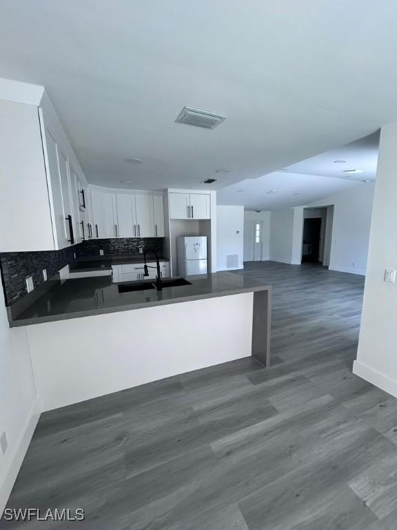 kitchen with tasteful backsplash, kitchen peninsula, sink, and white cabinets