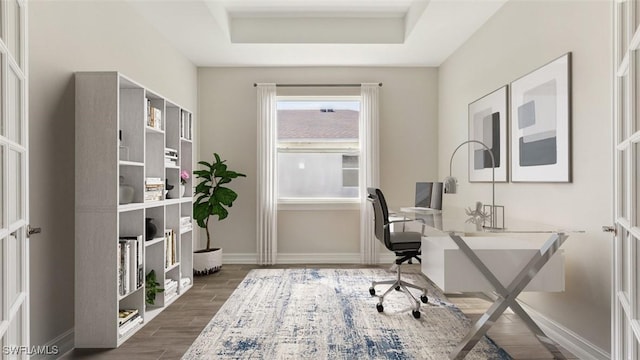 office area featuring wood finish floors, a raised ceiling, and baseboards