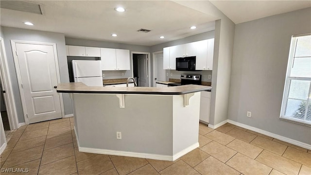 kitchen with stainless steel electric stove, white cabinets, a kitchen breakfast bar, white refrigerator, and a center island with sink