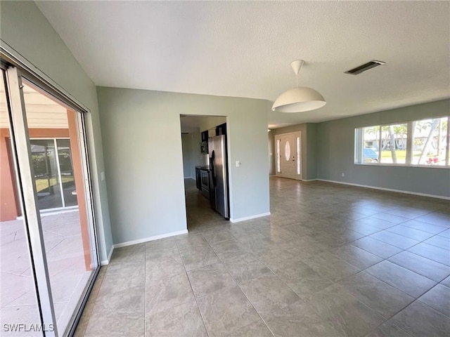 empty room featuring a textured ceiling, tile patterned floors, visible vents, and baseboards