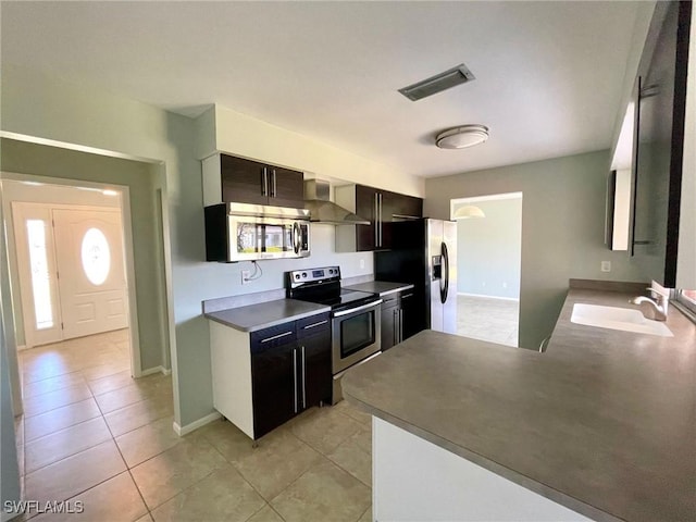 kitchen featuring visible vents, appliances with stainless steel finishes, light tile patterned flooring, a sink, and wall chimney range hood