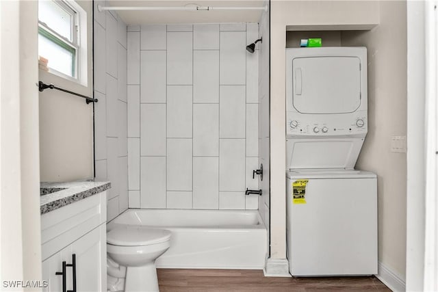 full bathroom featuring hardwood / wood-style floors, stacked washer and clothes dryer, vanity, tiled shower / bath combo, and toilet