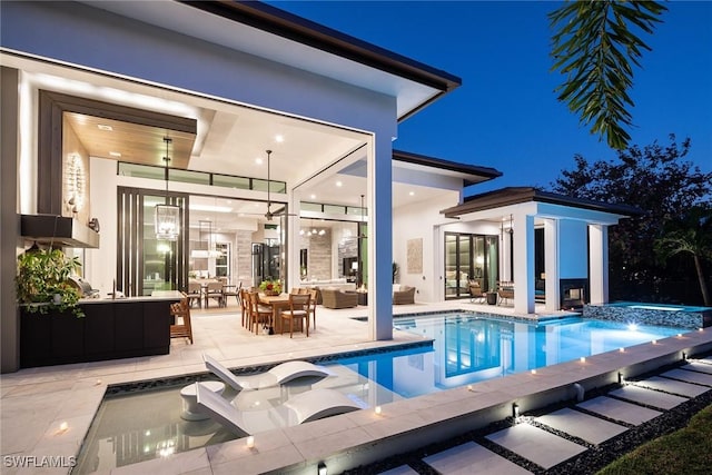 pool at night with an in ground hot tub, outdoor lounge area, and a patio