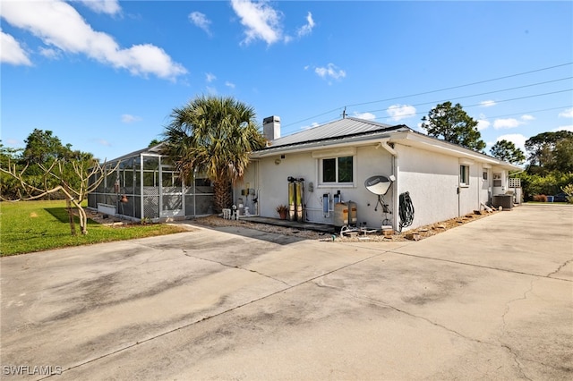 view of front facade featuring a chimney, stucco siding, a front yard, glass enclosure, and driveway