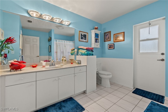 bathroom with a wainscoted wall, visible vents, toilet, vanity, and tile patterned flooring