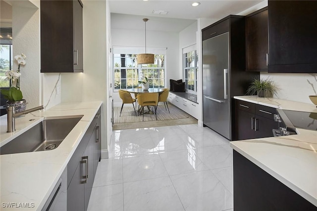 kitchen featuring sink, dark brown cabinets, light stone counters, decorative light fixtures, and built in fridge