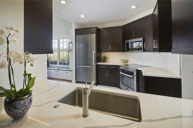 kitchen with appliances with stainless steel finishes, light stone countertops, sink, and dark brown cabinets