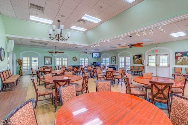 dining area featuring french doors, light wood-type flooring, track lighting, a notable chandelier, and a drop ceiling