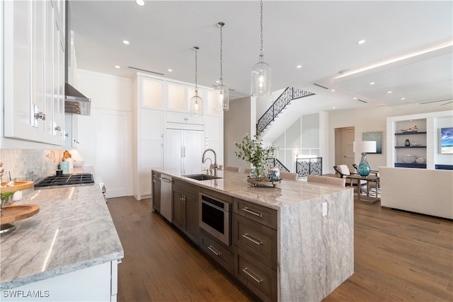 kitchen featuring pendant lighting, sink, stainless steel appliances, white cabinets, and a center island with sink