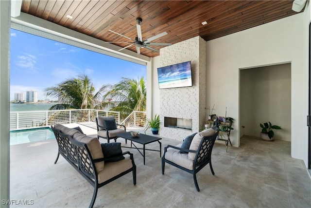 view of patio with a water view, ceiling fan, and an outdoor living space with a fireplace