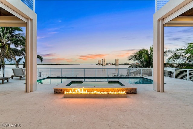 pool at dusk featuring an in ground hot tub, a water view, and a patio area