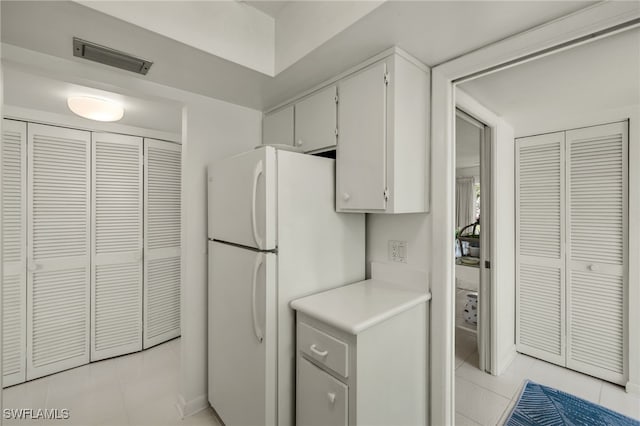 kitchen featuring light tile patterned floors, visible vents, white cabinetry, light countertops, and freestanding refrigerator