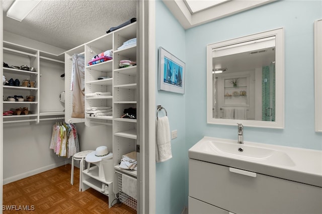 bathroom featuring a textured ceiling, a skylight, a sink, visible vents, and baseboards