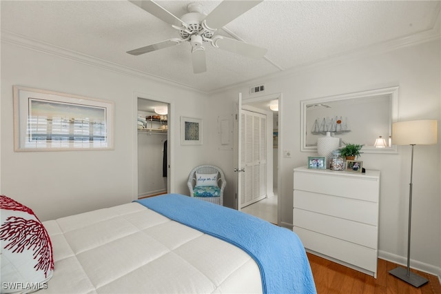 bedroom with visible vents, ornamental molding, a ceiling fan, a textured ceiling, and wood finished floors