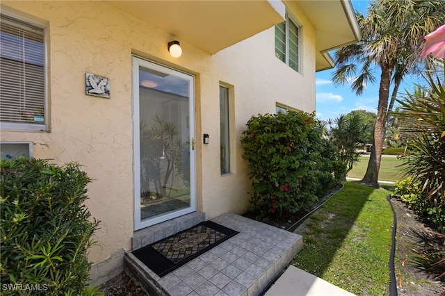 doorway to property with a lawn and stucco siding