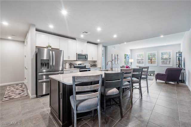 kitchen featuring a breakfast bar, light countertops, appliances with stainless steel finishes, a sink, and an island with sink