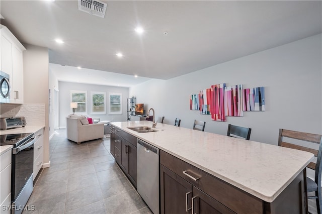 kitchen featuring stainless steel appliances, visible vents, open floor plan, a sink, and dark brown cabinets