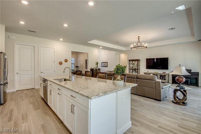 kitchen with sink, stainless steel appliances, light stone countertops, white cabinets, and a center island with sink