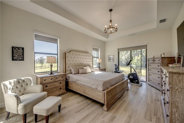 bedroom featuring light hardwood / wood-style flooring, access to exterior, a chandelier, and a tray ceiling