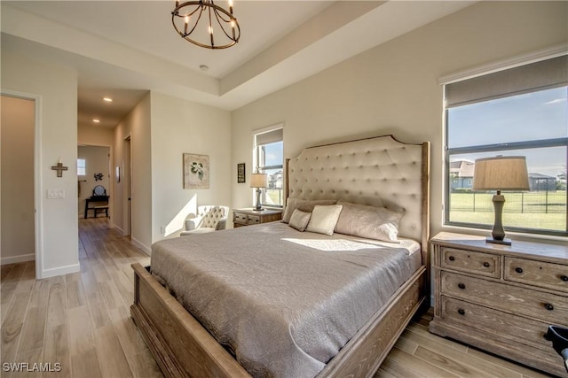 bedroom with an inviting chandelier, a raised ceiling, and light hardwood / wood-style flooring