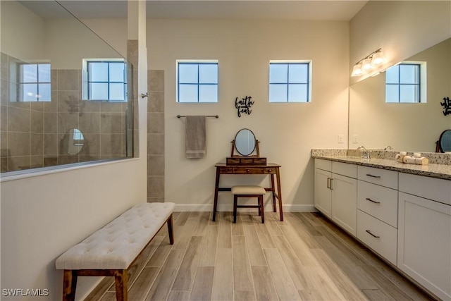 bathroom with a tile shower, vanity, and wood-type flooring