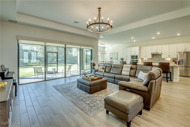 living room with a notable chandelier, light hardwood / wood-style flooring, and a raised ceiling