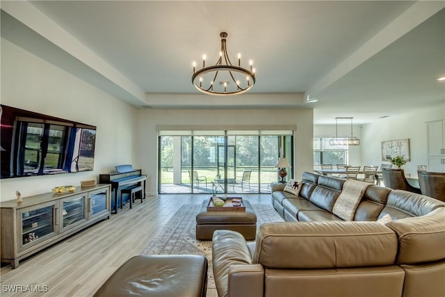 living room featuring an inviting chandelier, a raised ceiling, and light wood-type flooring