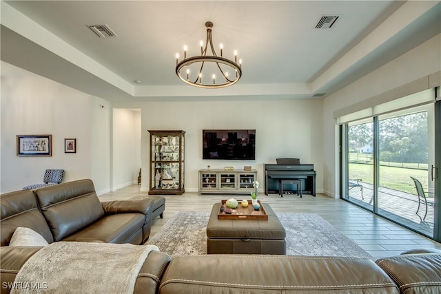 living room with a chandelier, a raised ceiling, and light hardwood / wood-style floors