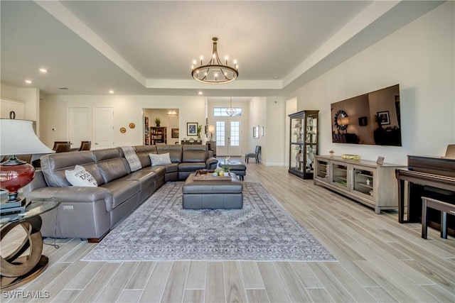 living room with light hardwood / wood-style floors, a tray ceiling, an inviting chandelier, and french doors