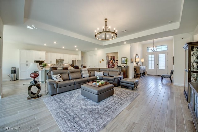 living room with french doors, a raised ceiling, light hardwood / wood-style floors, and a notable chandelier