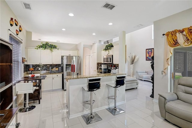 kitchen featuring white cabinetry, backsplash, a kitchen breakfast bar, stainless steel appliances, and light stone countertops