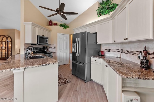 kitchen with a peninsula, appliances with stainless steel finishes, white cabinets, and a sink