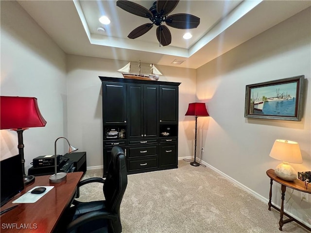 carpeted office with ceiling fan and a tray ceiling