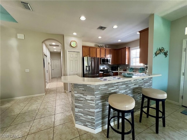 kitchen featuring light tile patterned flooring, a kitchen bar, tasteful backsplash, appliances with stainless steel finishes, and kitchen peninsula