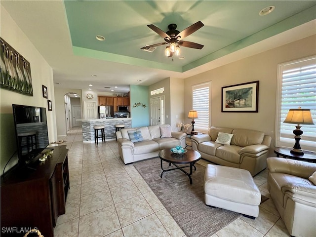 living room with a raised ceiling, ceiling fan, and light tile patterned flooring