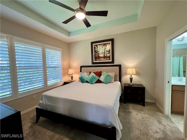 bedroom with ensuite bath, a tray ceiling, and light colored carpet