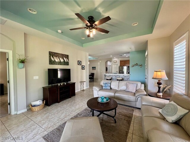 tiled living room with a tray ceiling and ceiling fan