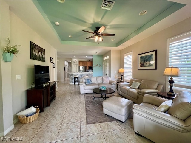 tiled living room with a tray ceiling and ceiling fan