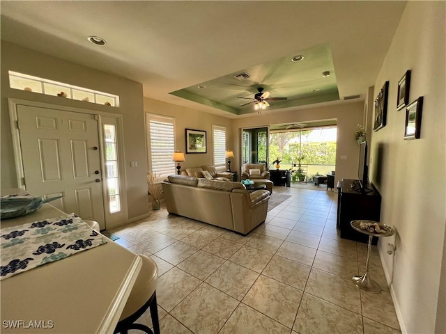 tiled living room with ceiling fan and a raised ceiling